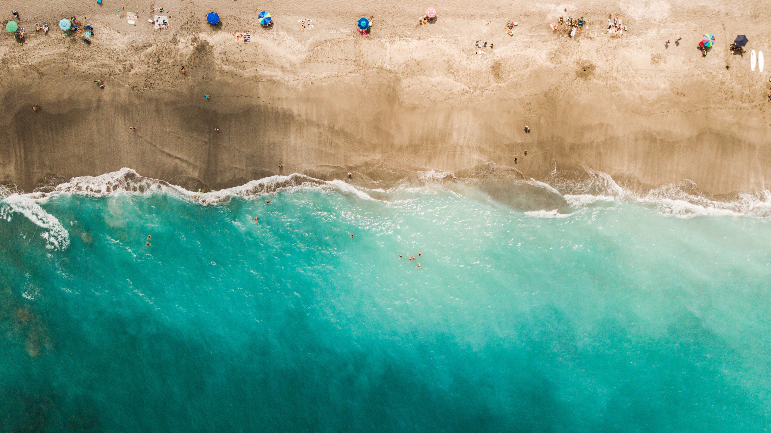 Direct Aerial Overview of a Vibrant Teal Ocean Seashore and Colorful Beach Umbrellas on Jupiter, Florida at Mid-Day During COVID-19 in April of 2021