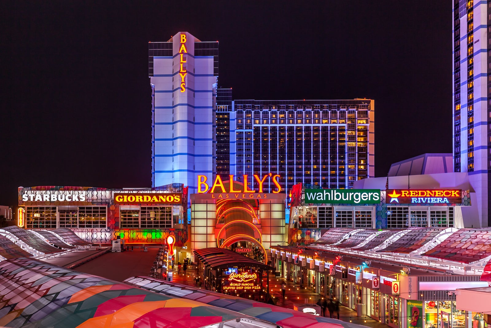 photo of large casino and hotel lit up purple with shopping center out front