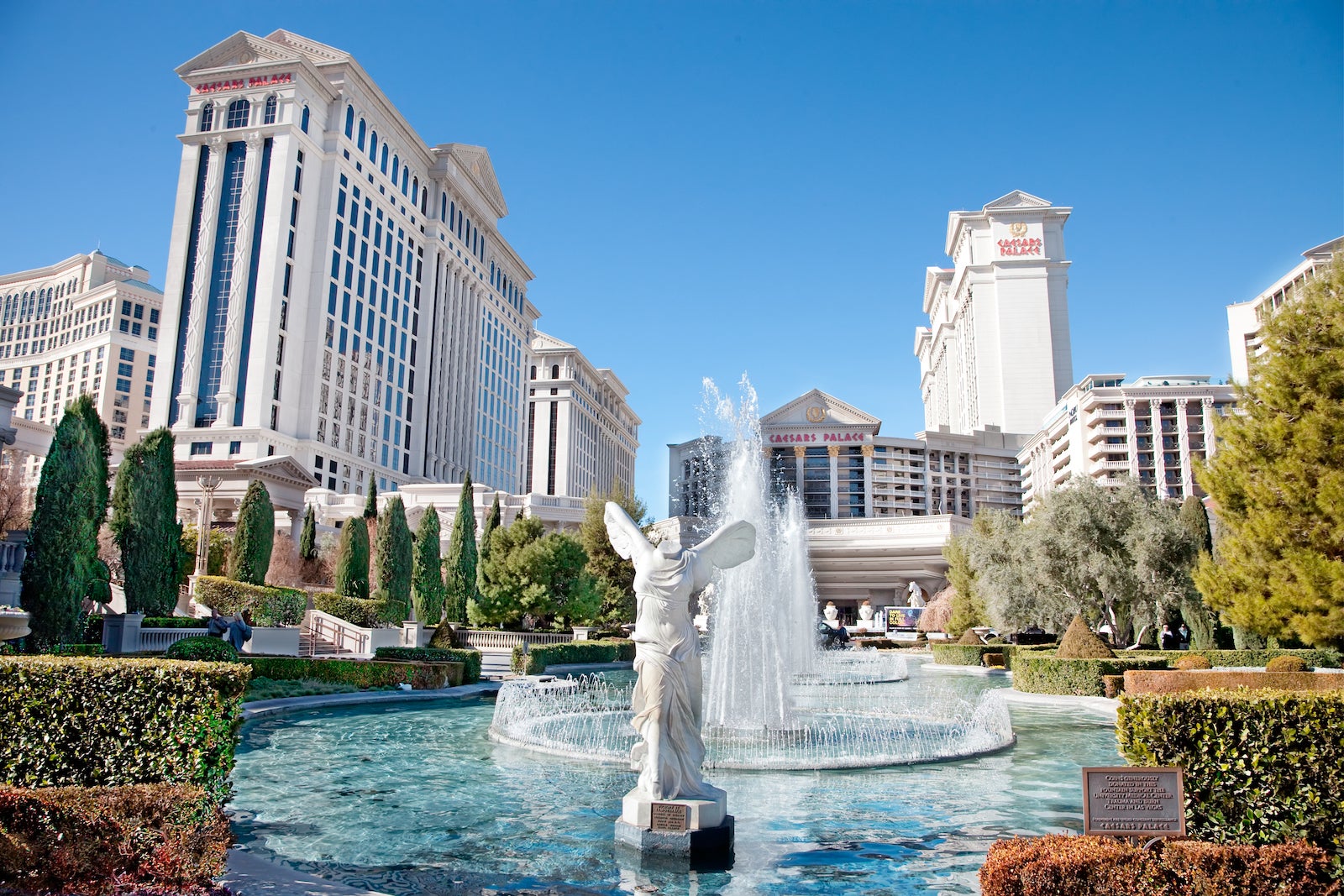 view of round fountain with angel statue in front of large Roman-style hotel towers