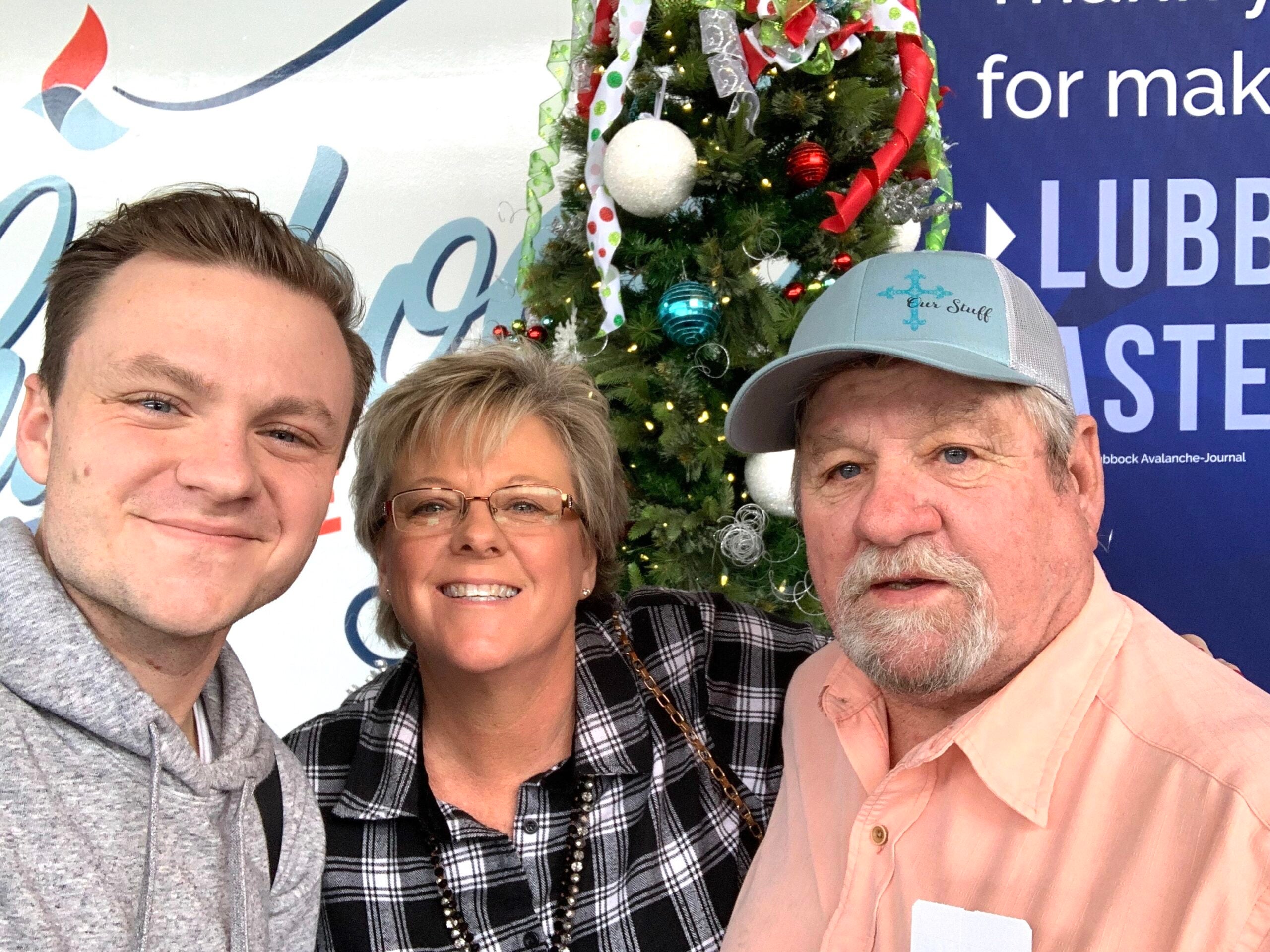 young man with parents in front of Christmas tree