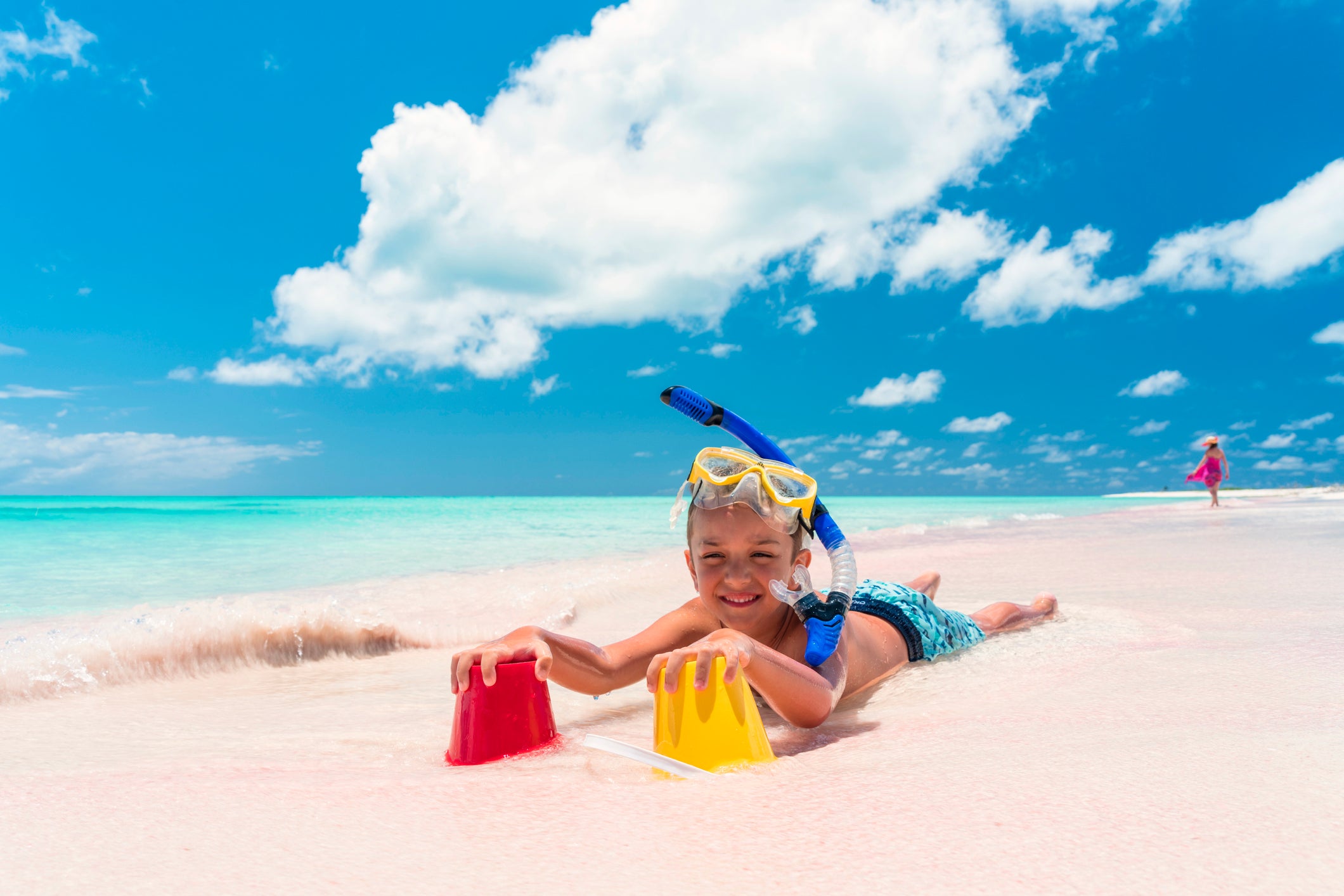 Boy wearing snorkel, lying in sand with sand toys
