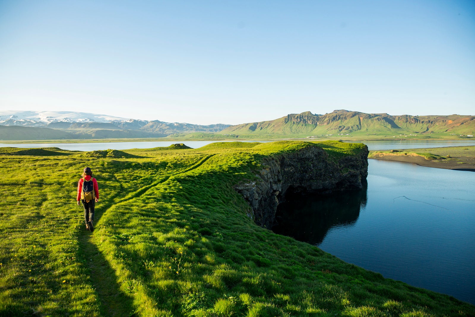 A woman hiking a lush scenic trail along a lagoon in Iceland.