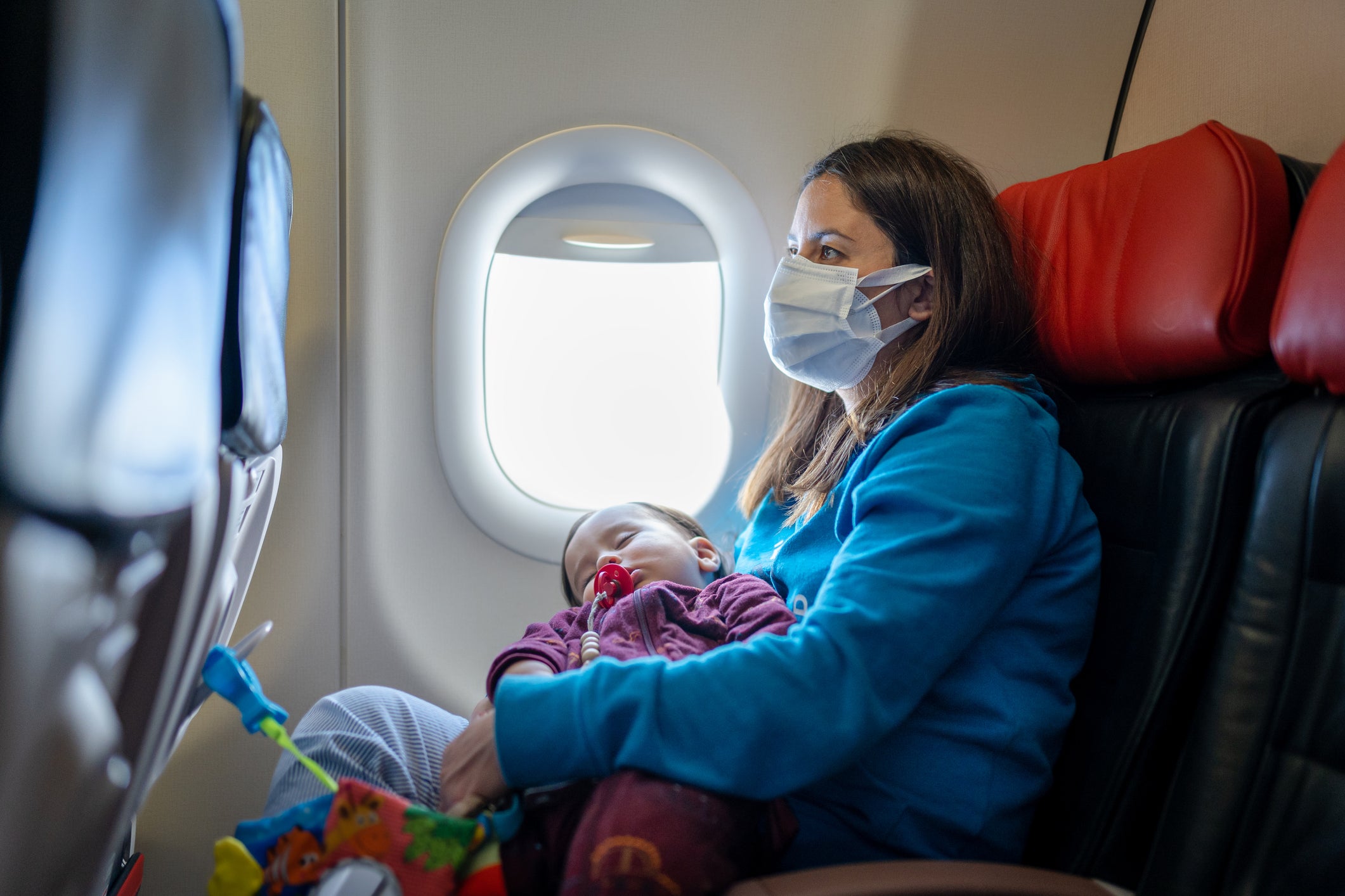 Young Woman traveling with her baby by plane wearing a face mask during the COVID-19 pandemic