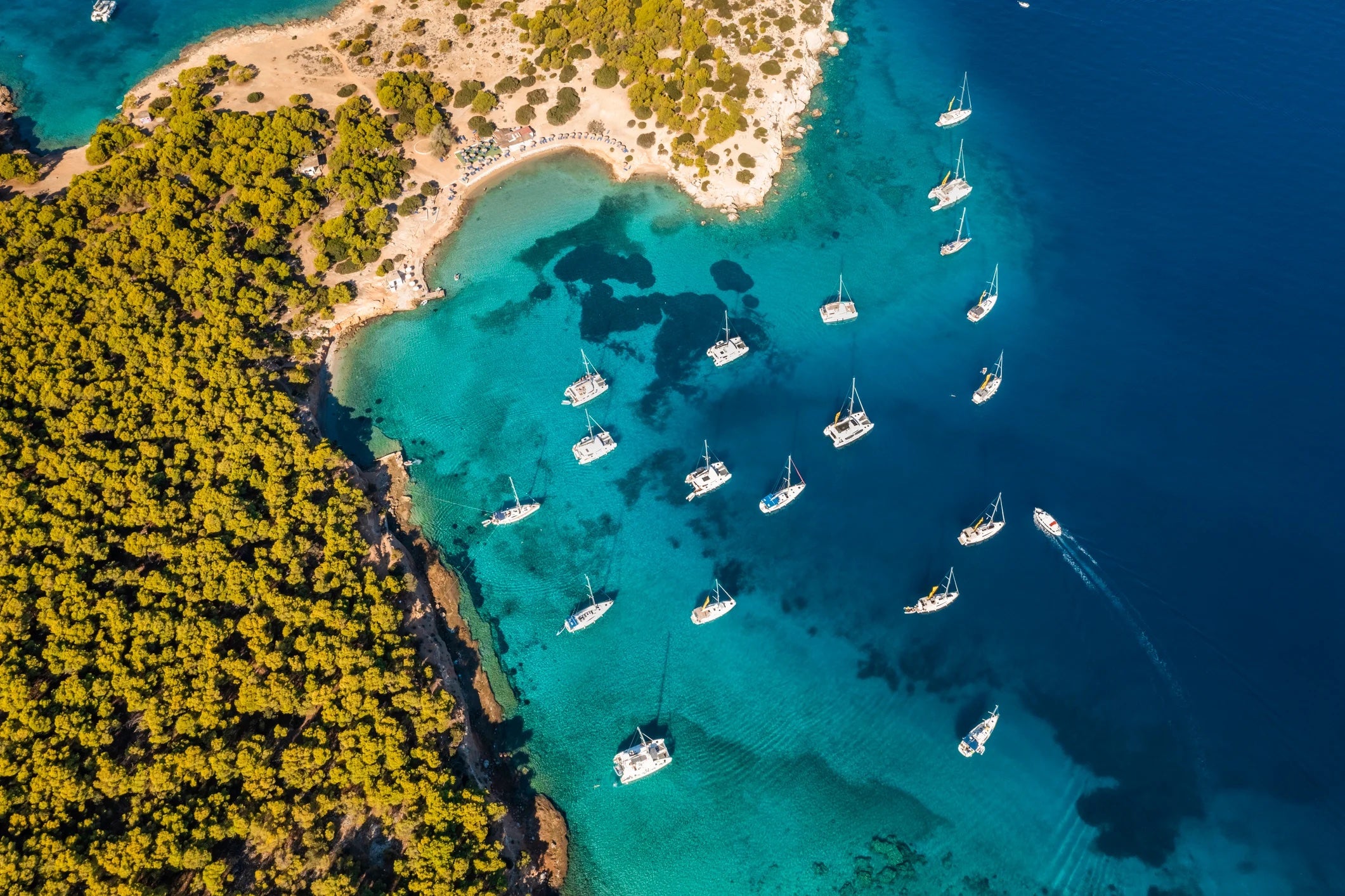 Yachts in turquoise water near the green island of Moni Eginas, Greece.