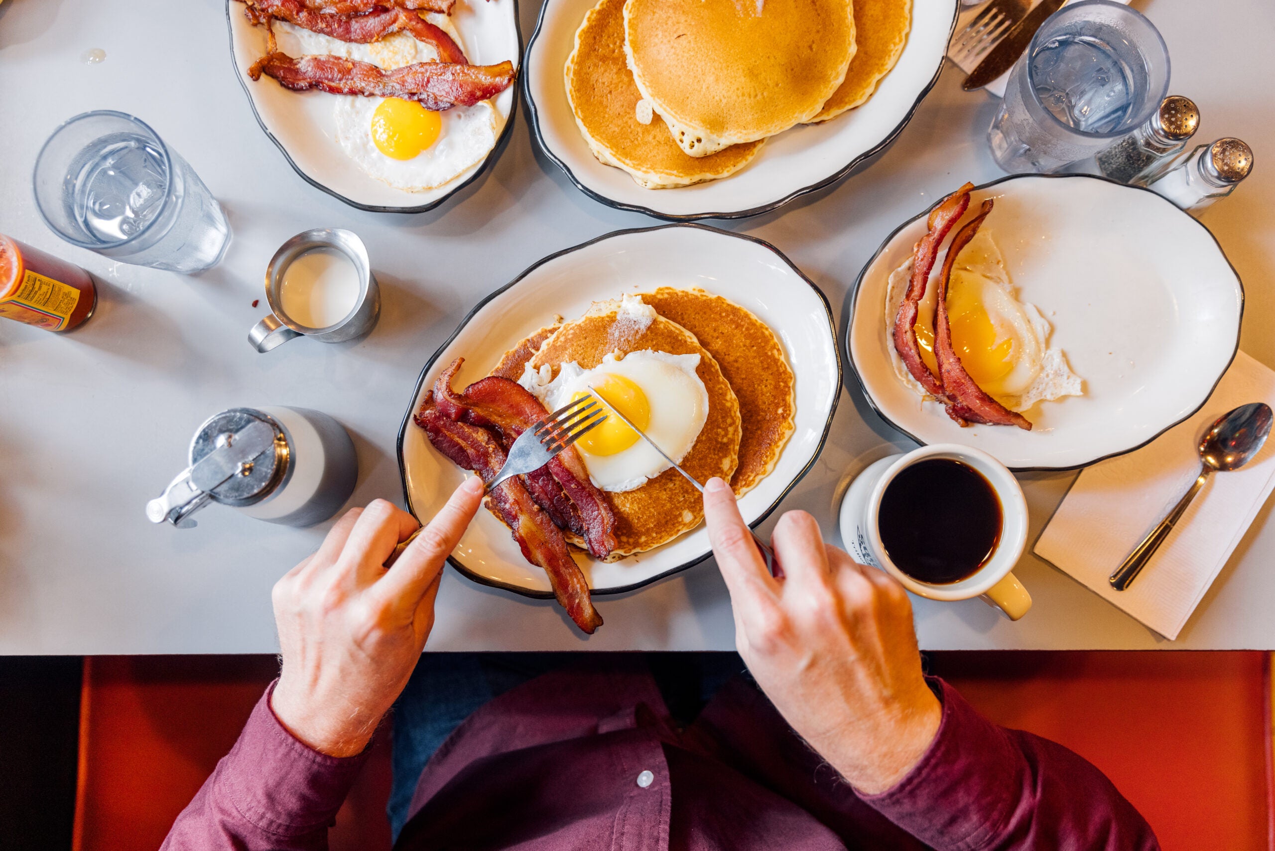 Man eating pancakes with bacon and eggs in a traditional American diner, personal perspective overhead view