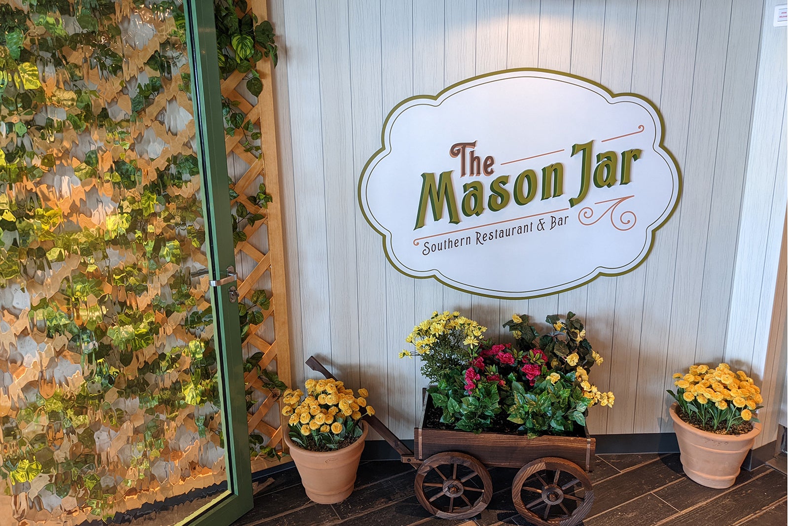 Sign reading Mason Jar above wooden wheelbarrow with flowers