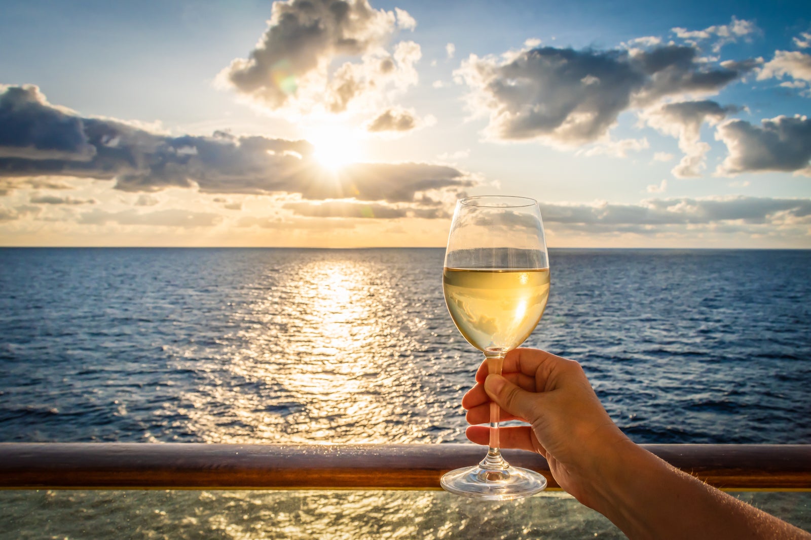 A glass of white wine in a female hand at sunset on cruise vacation.