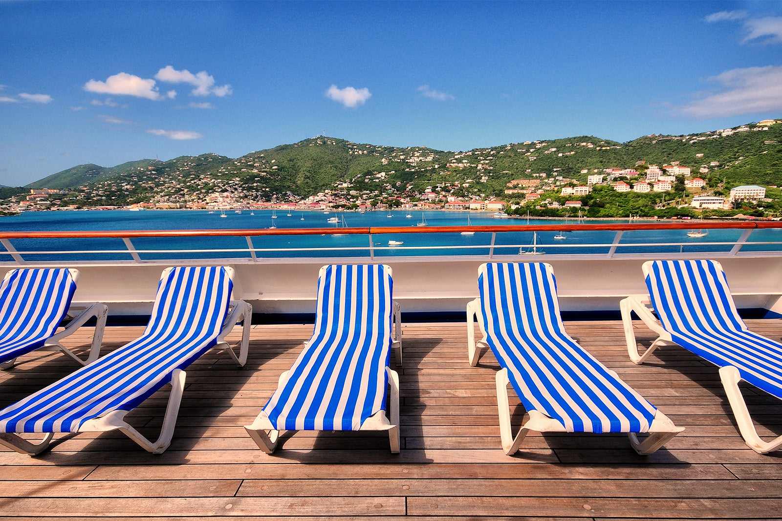 Empty lounge chairs on the top deck of a cruise ship overlooking a tropical island in the Caribbean
