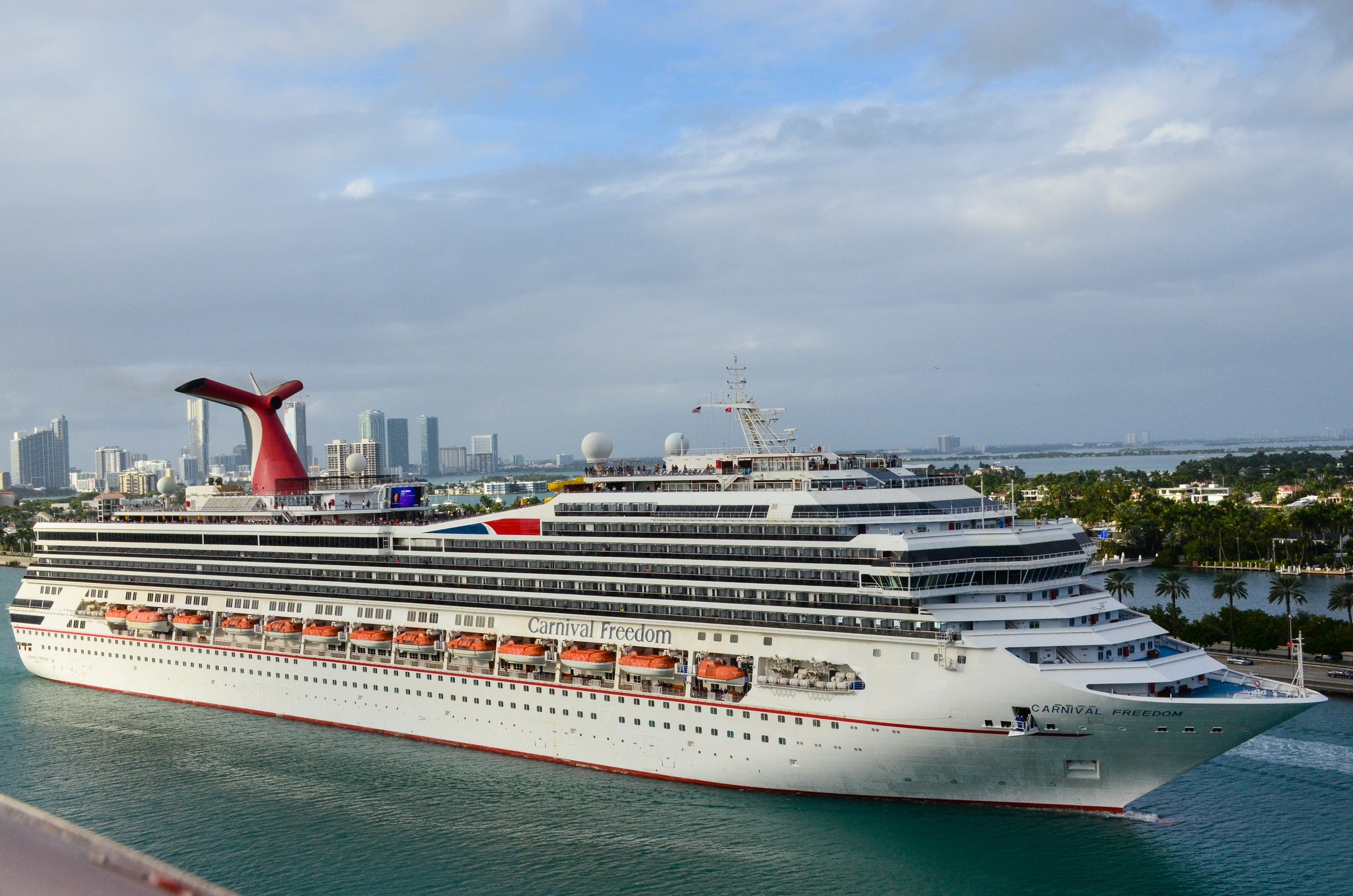 Carnival Freedom cruise ship sailing out to sea with Miami Beach skyline in the background at Port of Miami.