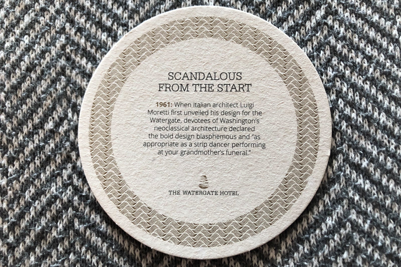 On a drink tray by the bed, several coasters featuring historical context about The Watergate Hotel's architecture can be found.