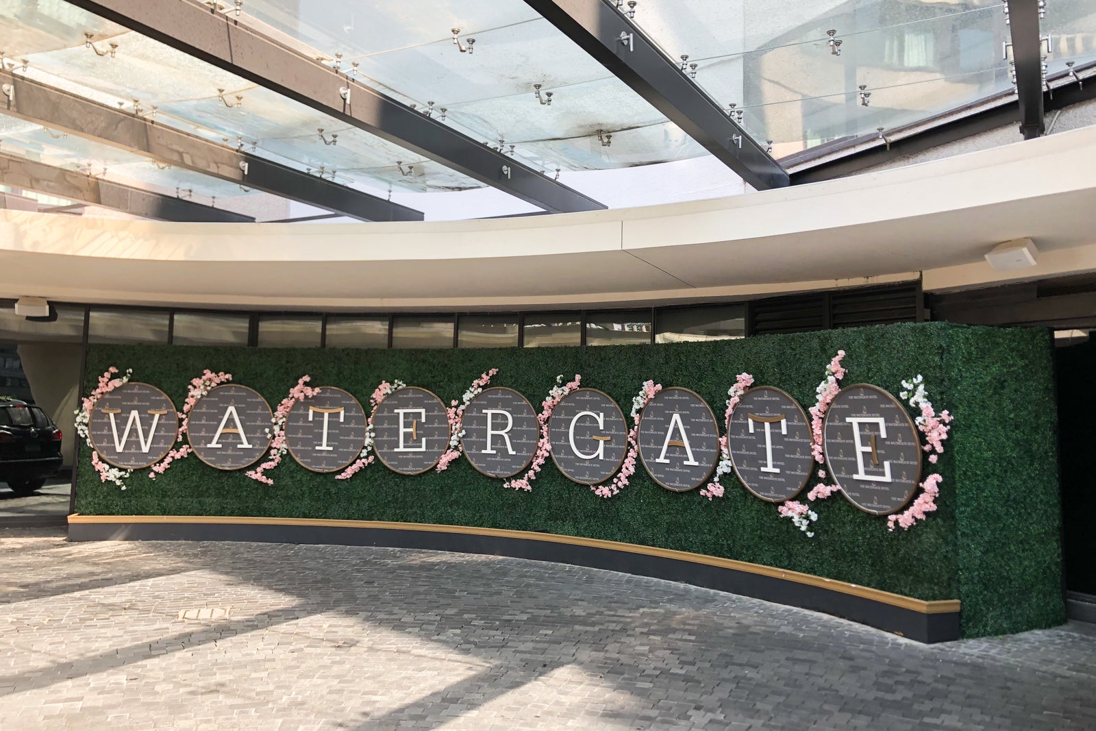 A break from the drab concrete exterior of the Watergate buildings, the faux grass hotel sign with pink floral accents provides a taste of the midcentury modern decor you'll find inside The Watergate Hotel.