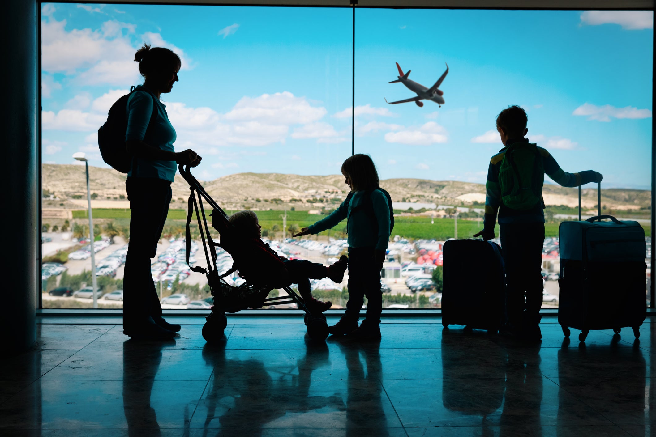 mother with kids and luggage looking at planes in airport
