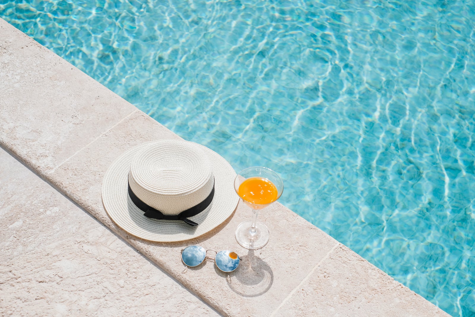 Fresh drink an orange juice, hat and glasses on the floor in front of pool in background in Koh Samui. Summer concept