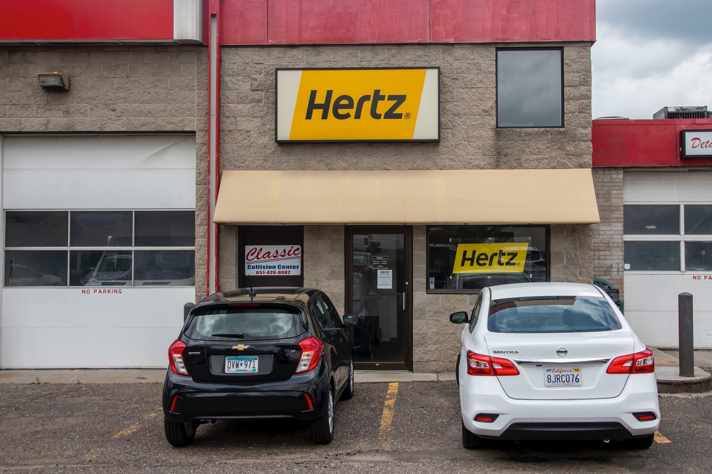 Two cars in front of a Hertz sign in a parking lot