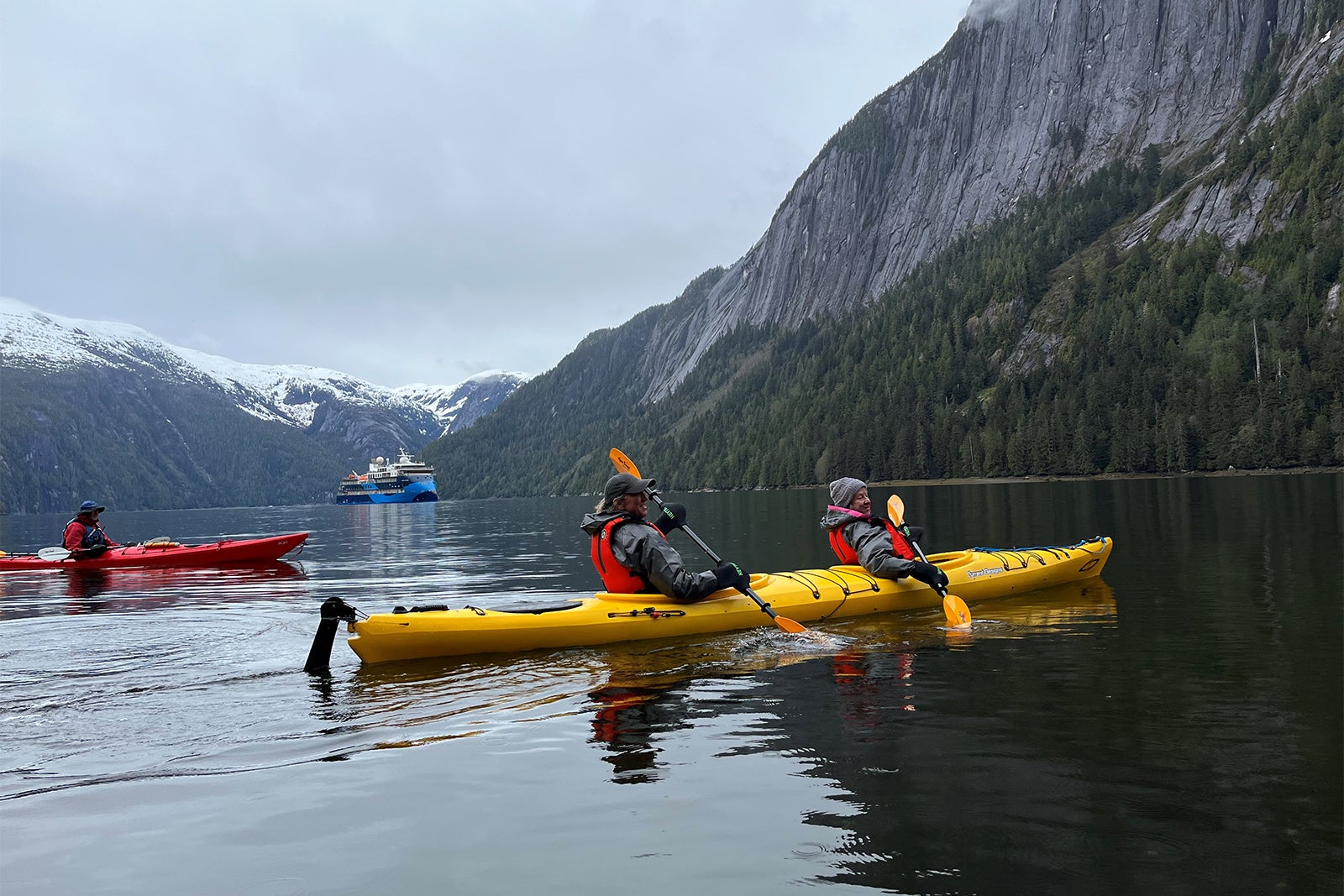 Cruise passengers kayak in Alaska with Ocean Victory cruise ship in the background.