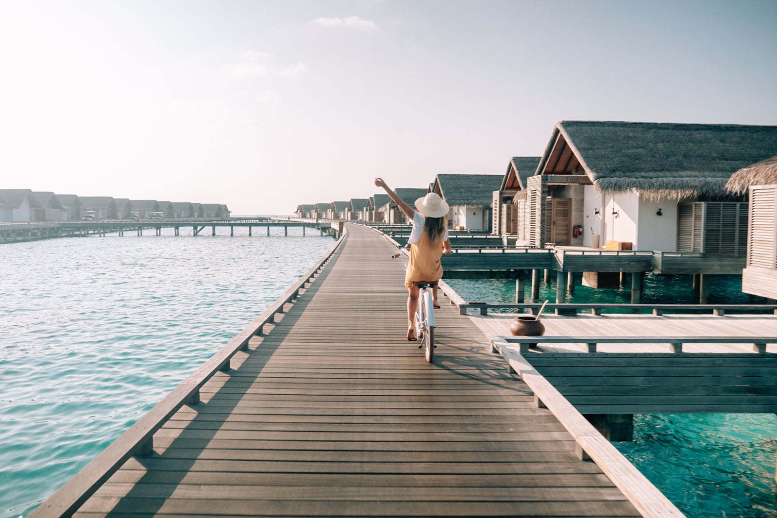 Tropical vacations, young woman with bicycle on wooden pier in the Maldives. Female enjoying bike ride on jetty over coral reef water. Dreamlike destination