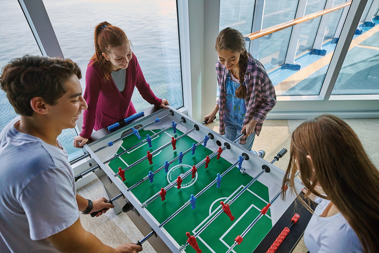 Four teens playing foosball with ocean views on Caribbean Princess cruise ship