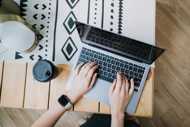 High angle view of woman using laptop on wooden desk, with a cup of coffee by her side. Lifestyle and technology. Staying connected throughout the city. Business on the go