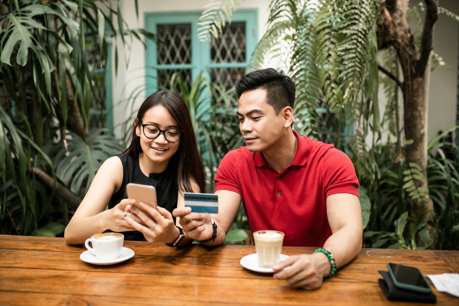Beautiful adult couple at cafe shopping online while man holds credit card both smiling