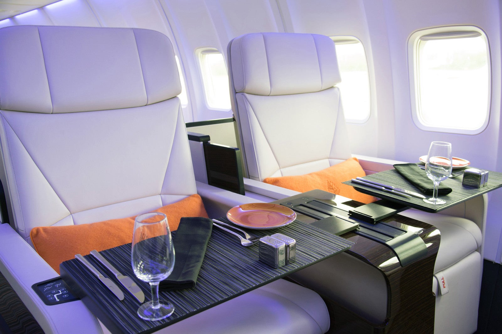 White leather airplane seats, foldout tables holding dishware