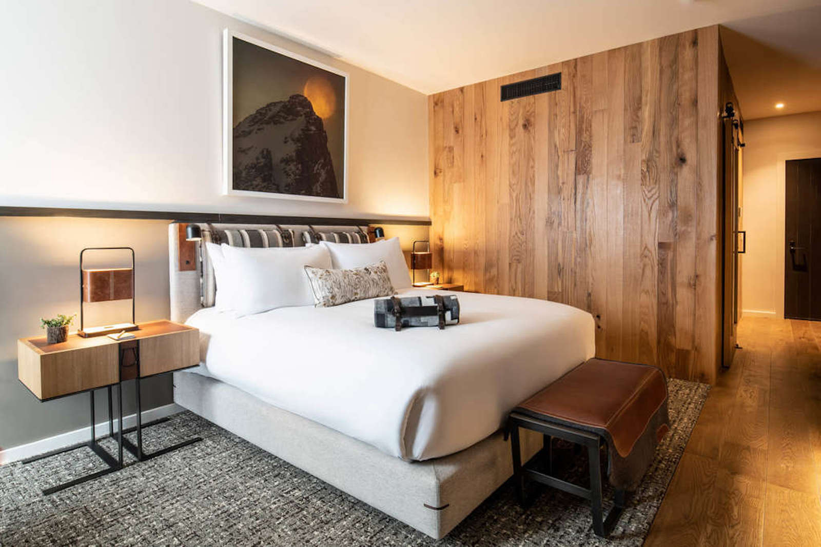 A hotel room with a wooden wall, a bed and a photo of a mountain above the bed