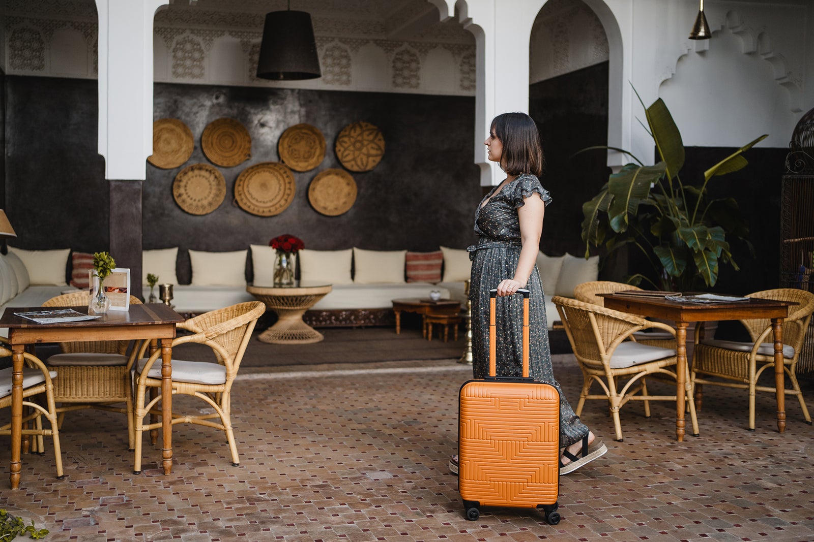 side view of young woman with an orange suitcase in the hotel