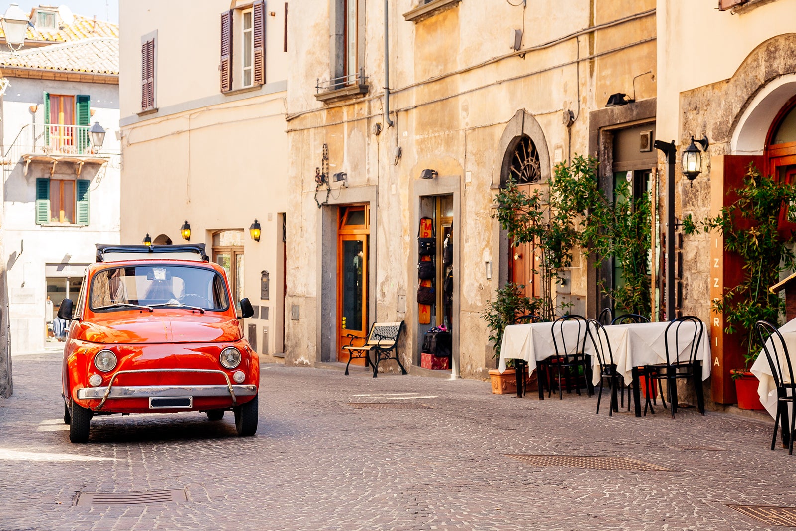 Old red small vintage car on the street of Italian city on a sunny day