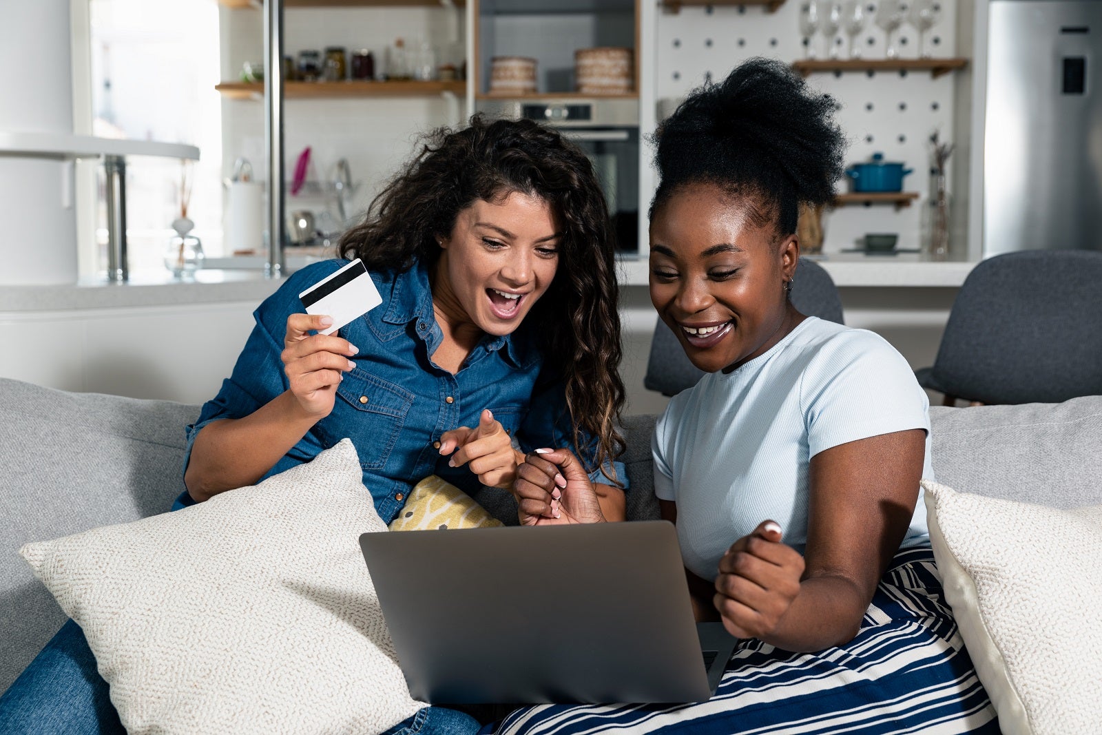 Two young happy women online buying a ticket for vacation and booking the hotel in touristic resort for holidays on laptop. Two female friends online shopping with credit card from their apartment.