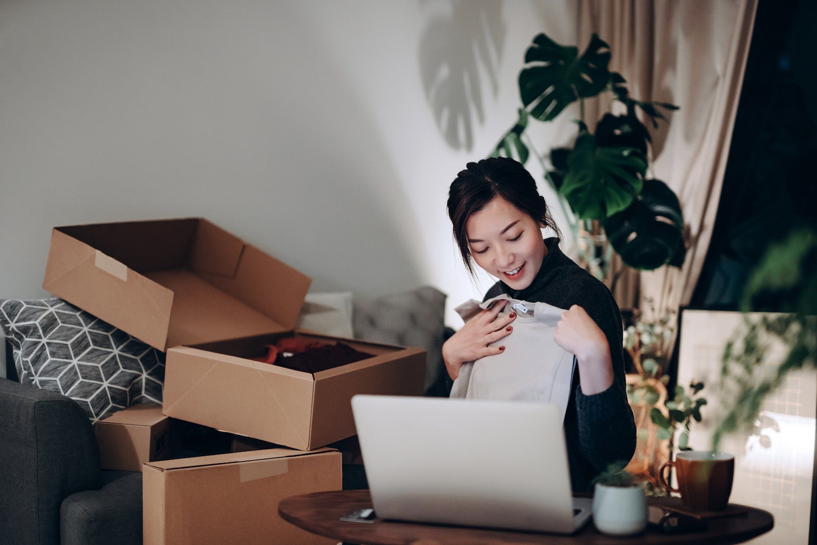 a young woman sits at her laptop with multiple boxes she received from online purchases