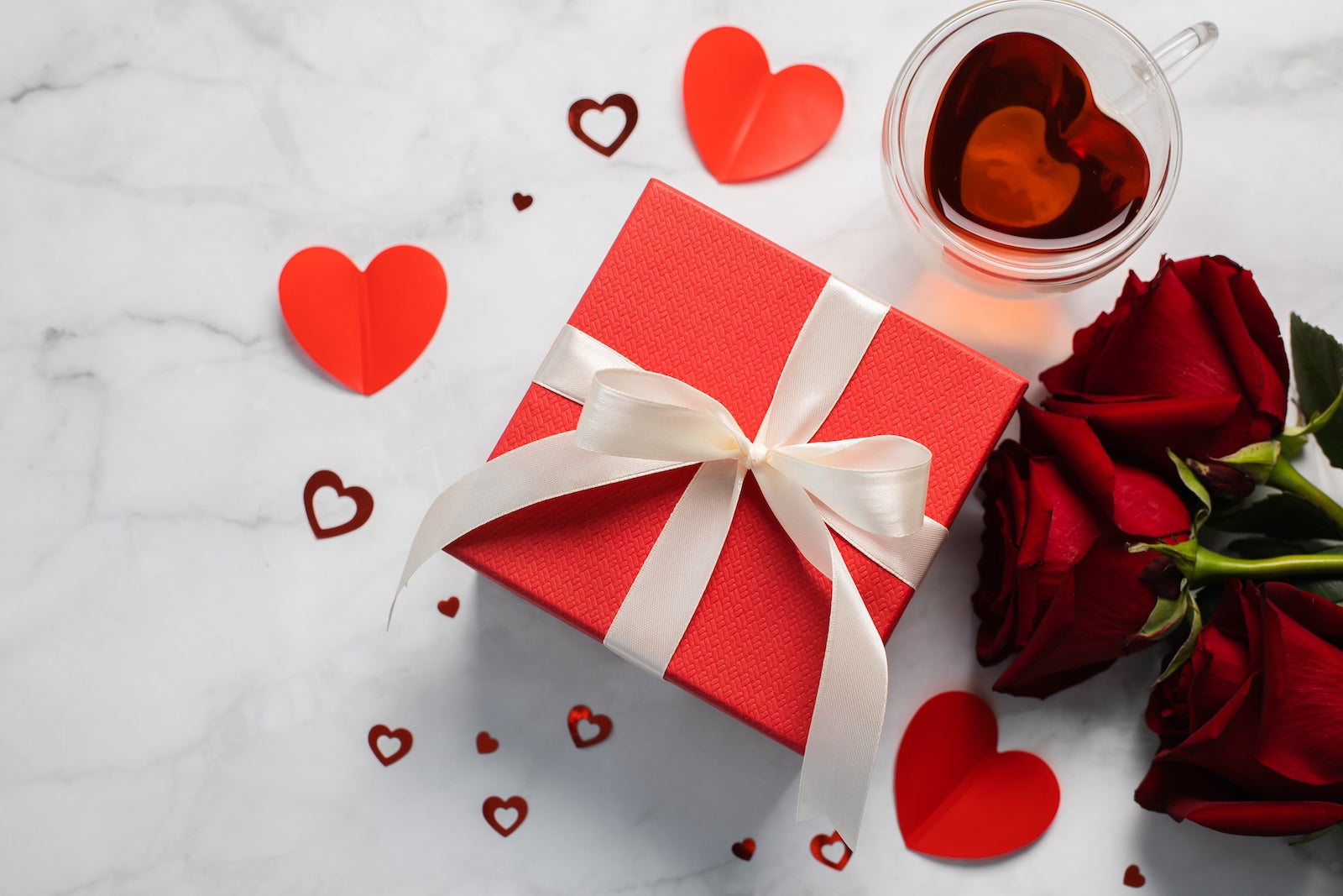 Red Valentine's Day gift box with roses and tea in the background