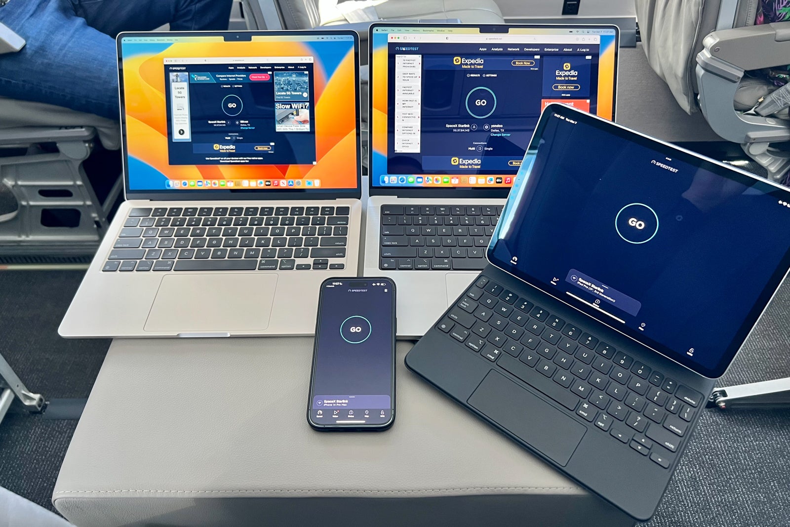 Three laptops resting on an airplane seat