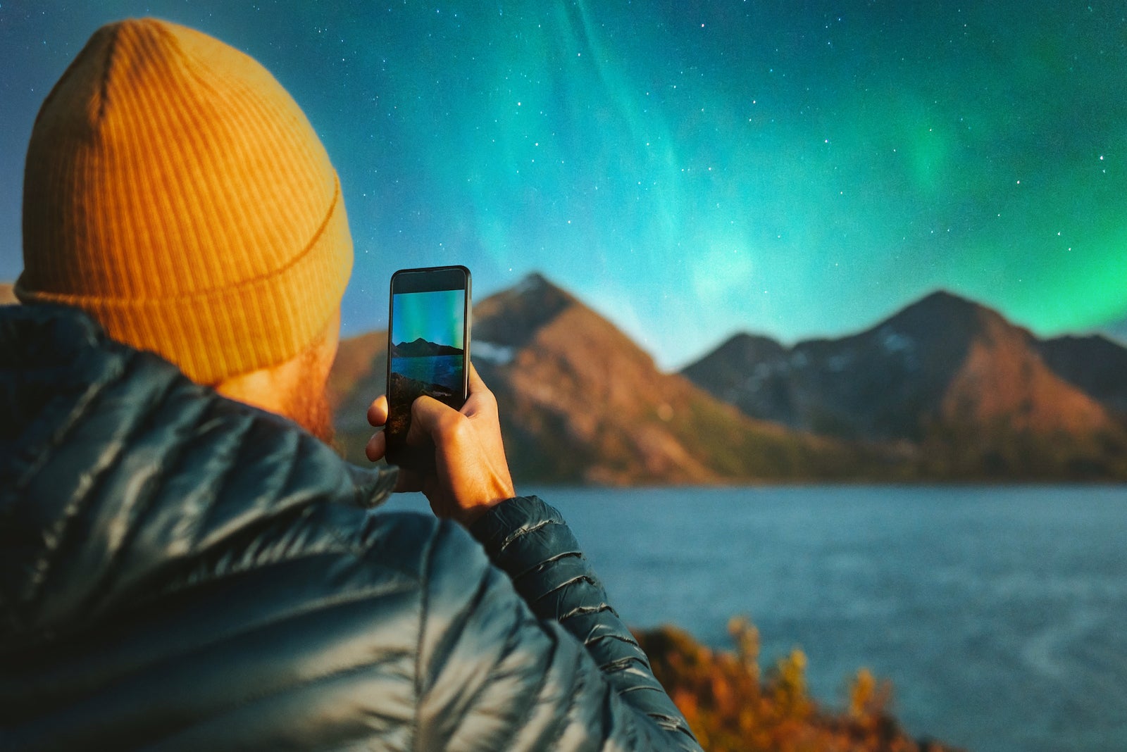 Man with smartphone taking photo of northern lights winter travel in Norway adventure vacations outdoor blogger influencer lifestyle modern online technology