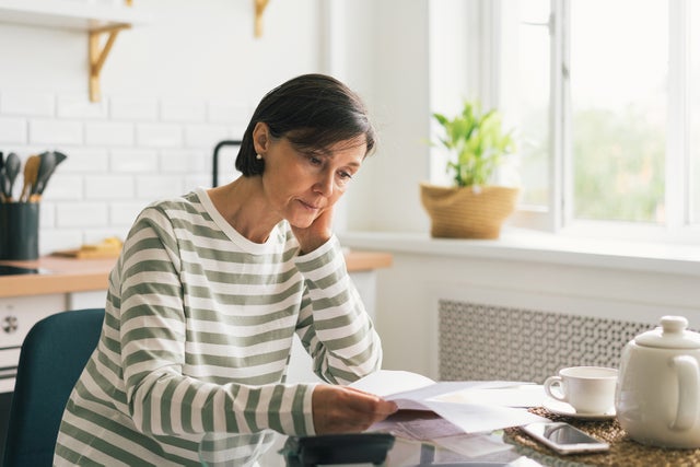 Upset woman thinking about high prices while looking at utilities, gas, electricity, rental charges, water bill due to inflation and crisis. Planning personal budget while sitting in kitchen. Weighing options on how to save money