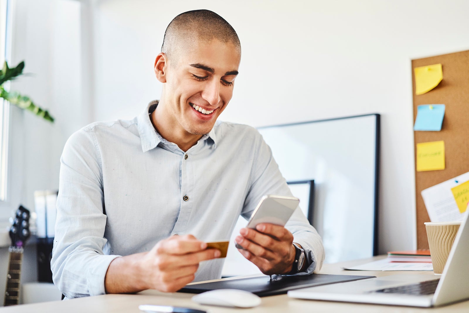 Young man sitting in home office paying online with credit card and smartphone