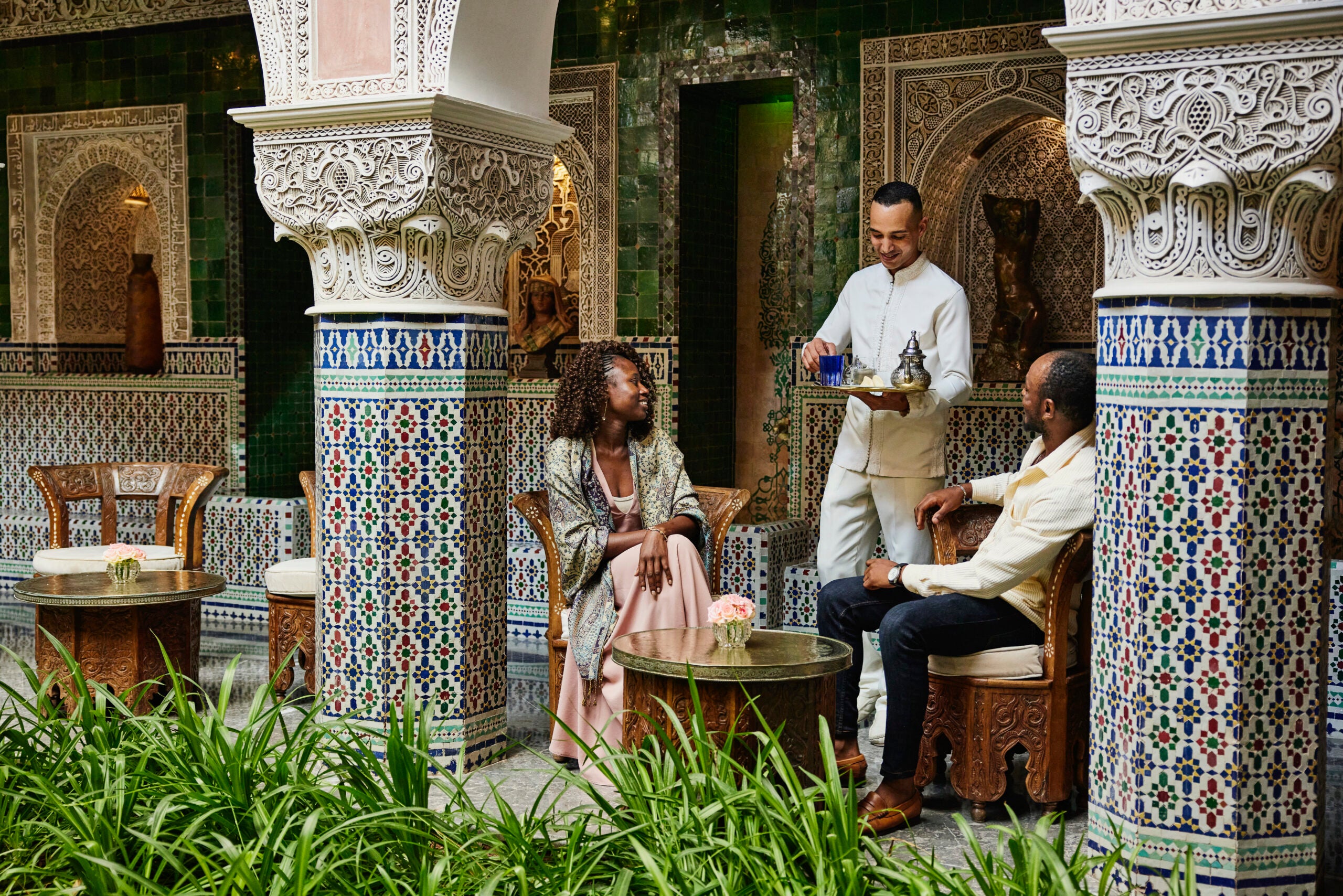 Wide shot of couple being served tea in courtyard of luxury hotel
