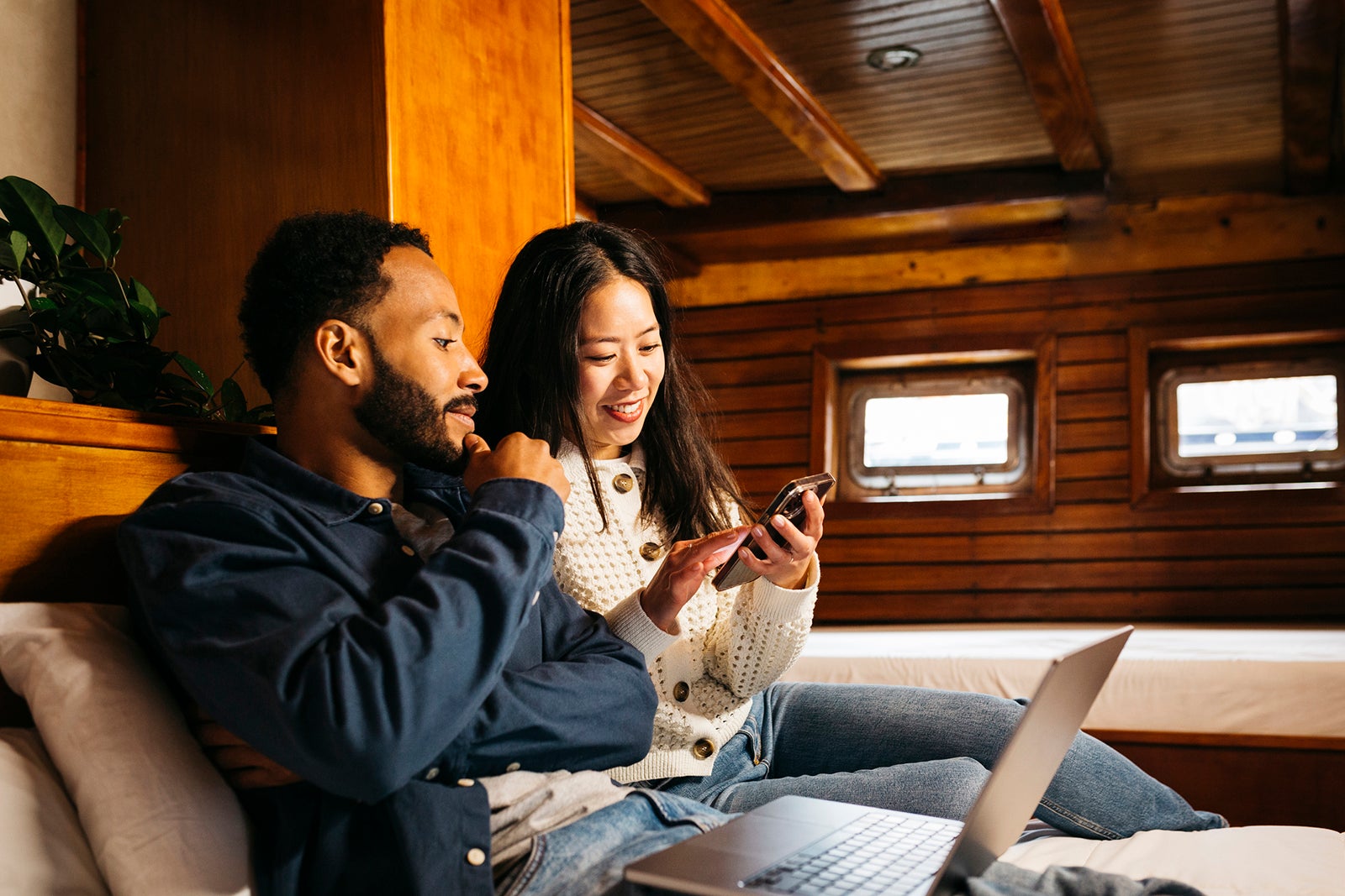 Couple using laptop in a sailing boat cabin