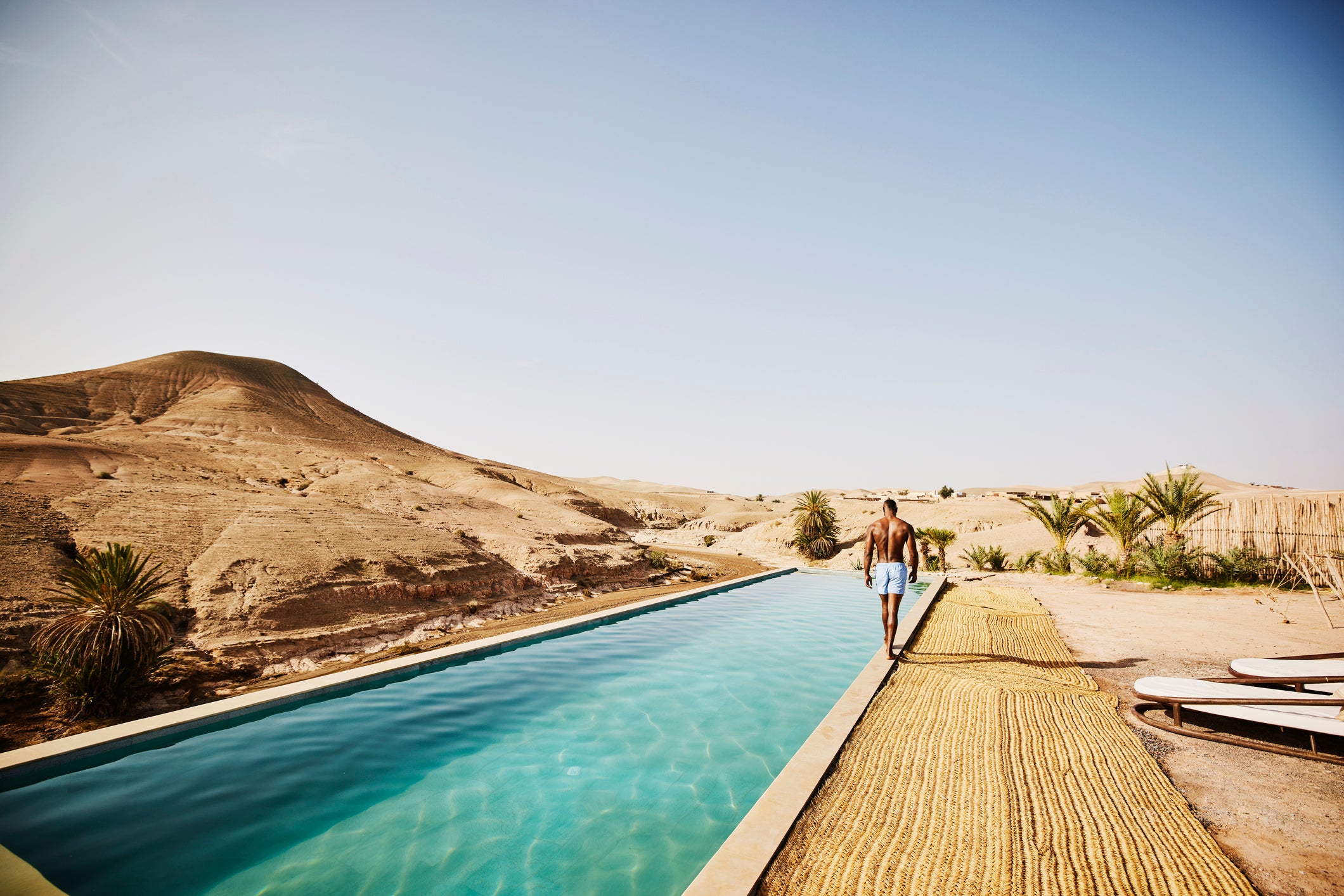 Wide shot of man walking around edge of pool at Moroccan desert camp