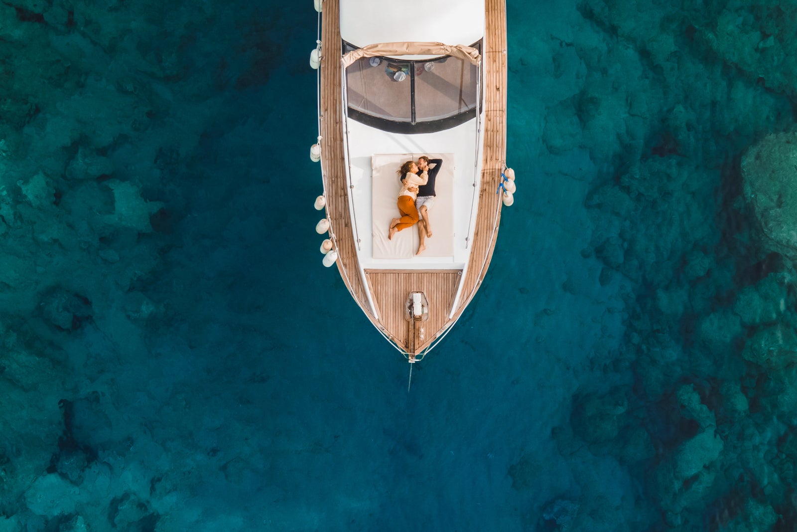 Aerial drone view of couple in love on board of luxury yacht anchored in tropical paradise bay with emerald clear water
