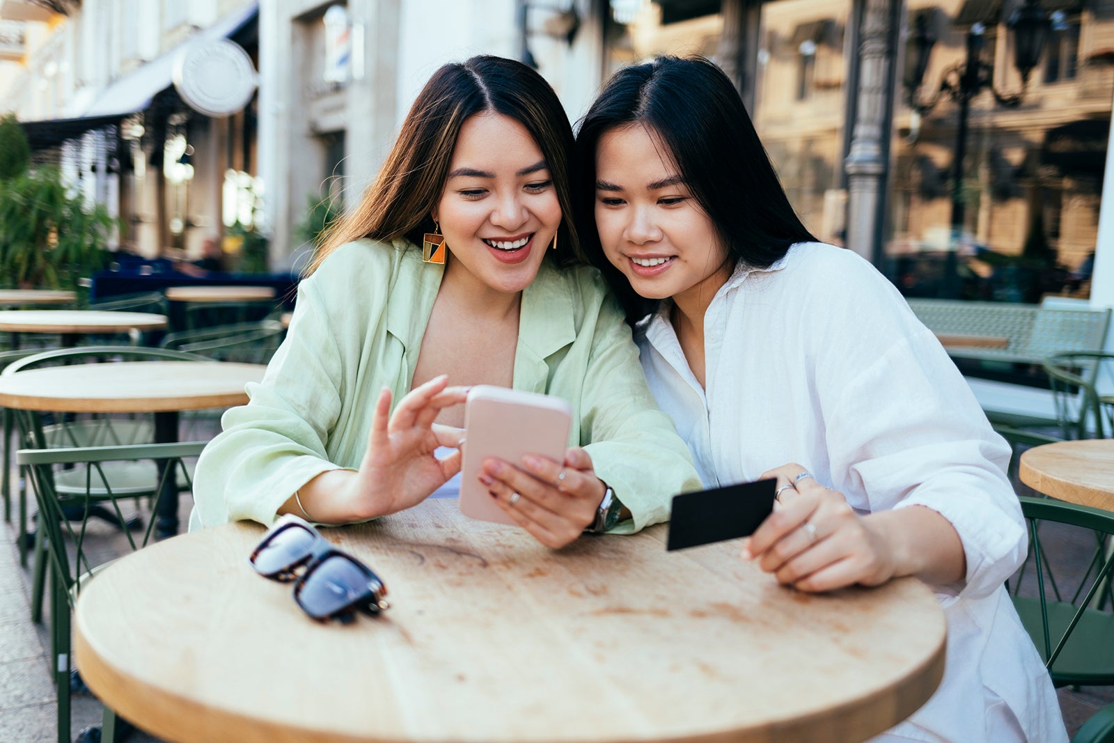 Smiling women shopping online through smart phone at sidewalk cafe