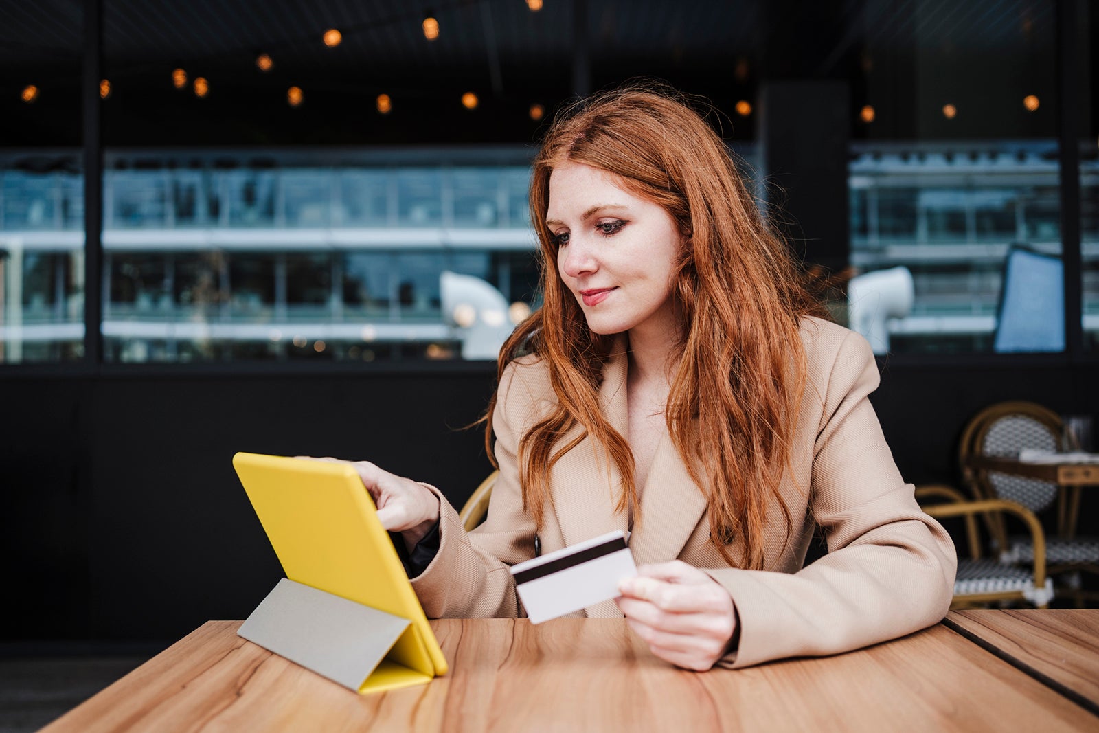 Redhead woman holding credit card while using digital tablet at cafe