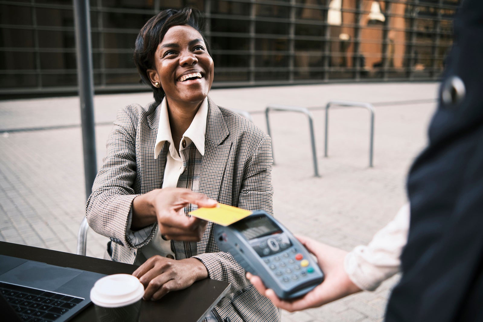 Cheerful businesswoman making payment with credit card to waitress at sidewalk cafe