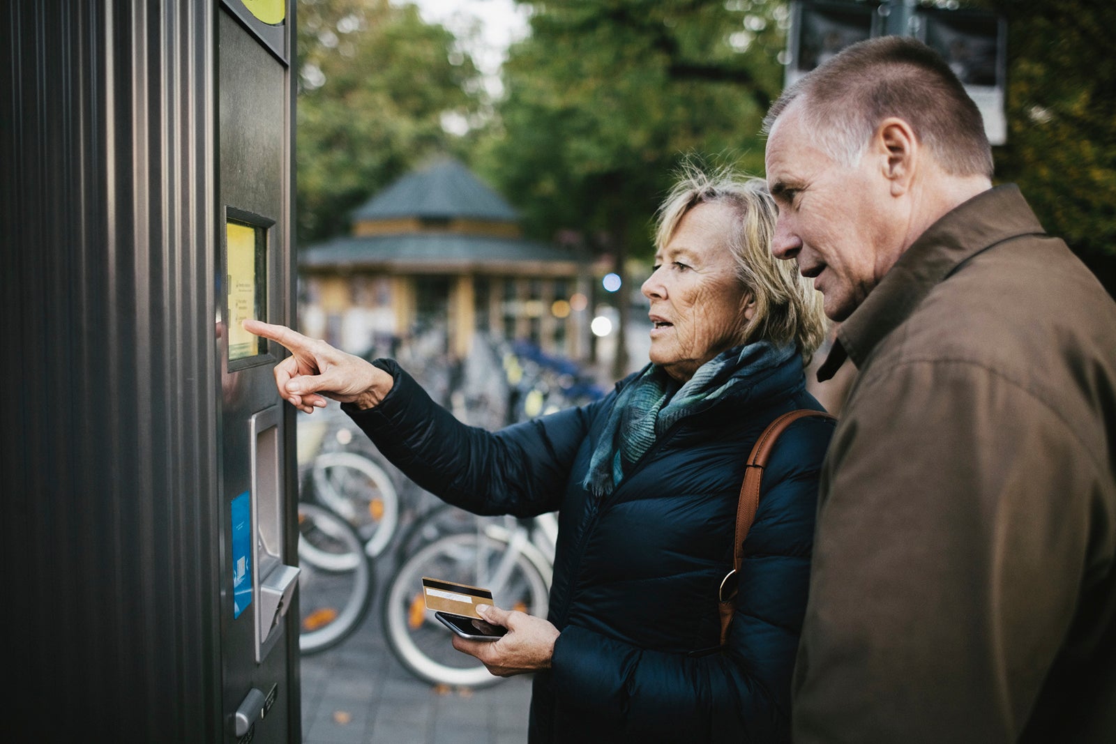 Senior man with woman making payment through credit card at bike rental station