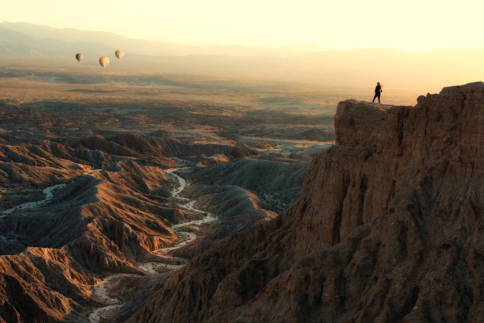 Woman standing on Font's Point looking at hot air balloons flying over badlands, Anza-Borrego Desert State Park, California, USA