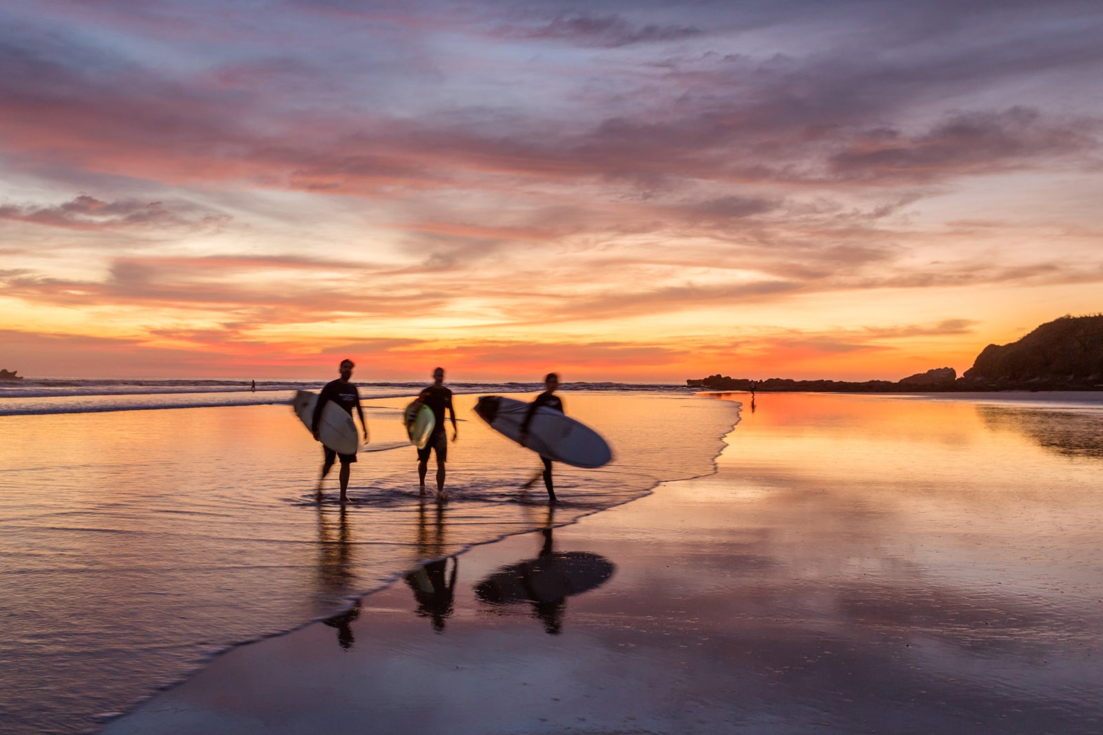 Surfers at sunset walking on beach, Costa Rica