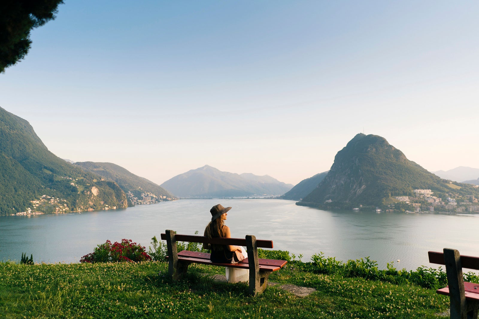 Woman relaxes above lake and mountains on bench