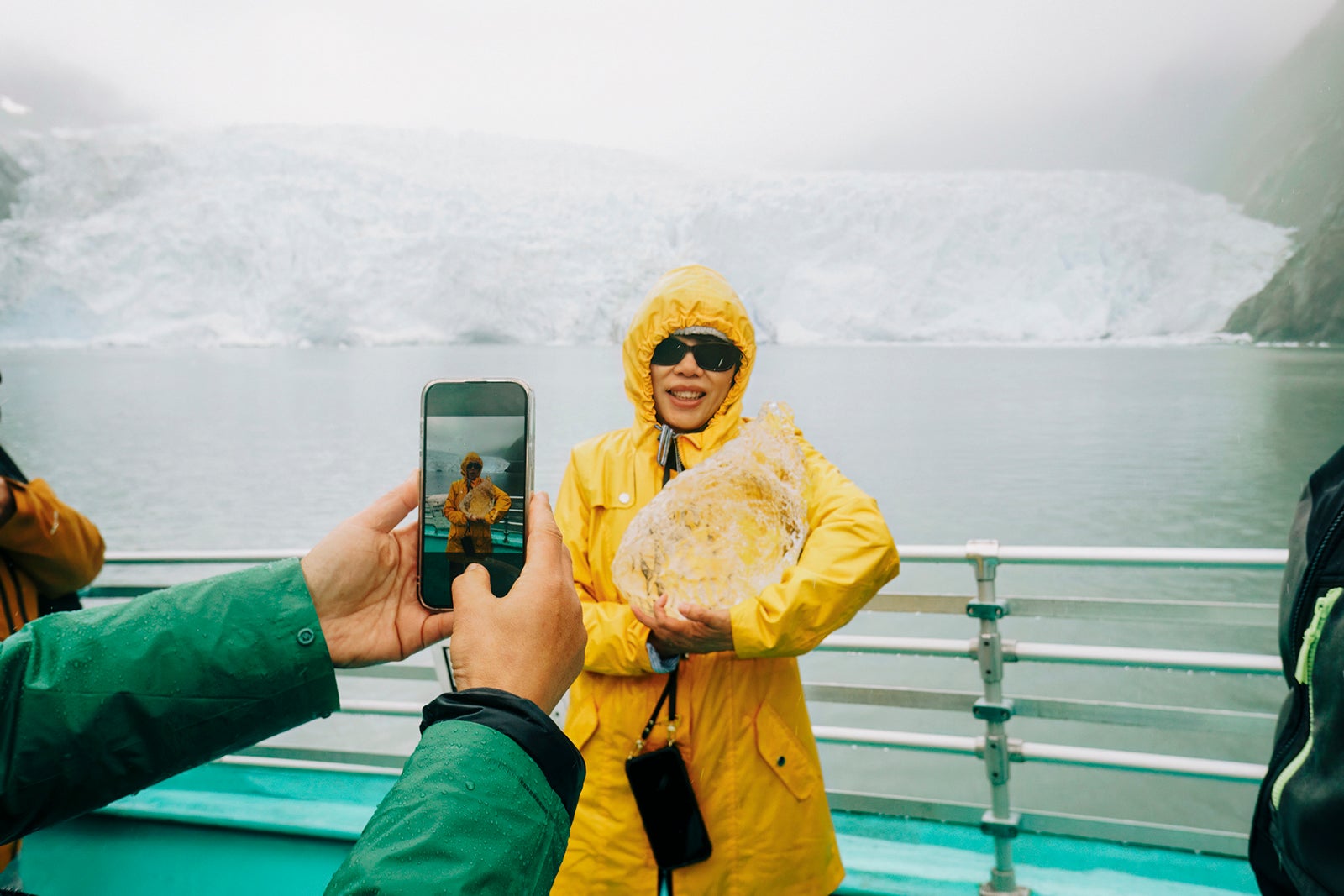 Tourist taking smartphone photos of a woman holding ice from an iceberg. Holgate Glacier in the rain. Kenai Fjords National Park. Seward. Alaska.