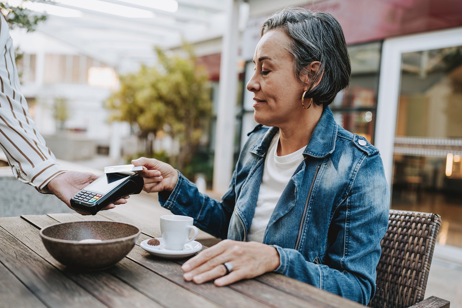 Woman sitting outside paying for coffee at cafe with contactless credit card payment andreswd