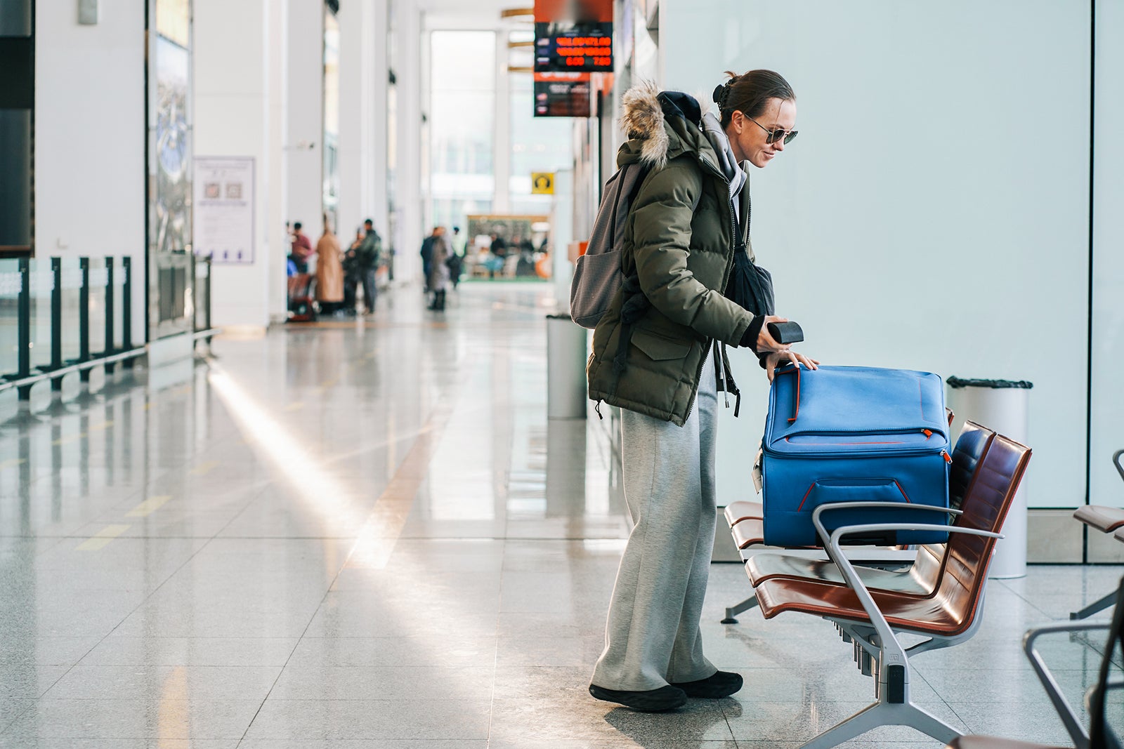 A woman in a jacket with a suitcase at the airport, front view, the woman looking for something in her luggage, the concept of forgetting things, checking luggage, winter travel with copy space.