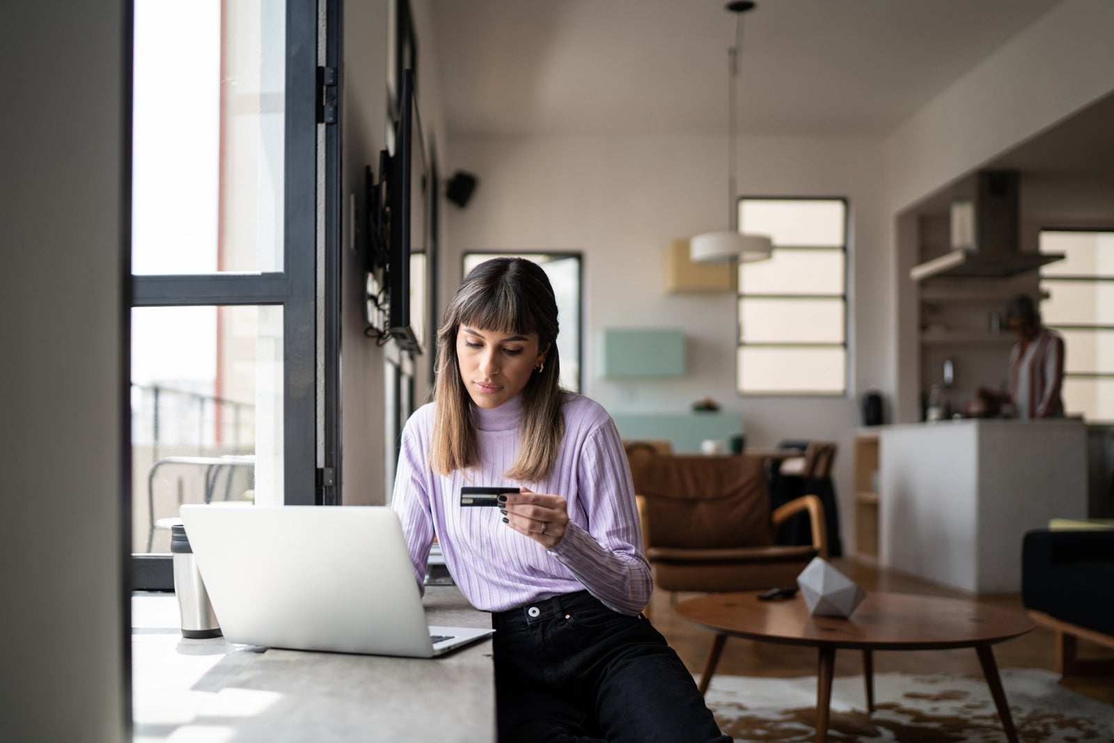 Young woman holding credit card while using laptop at home FG Trade