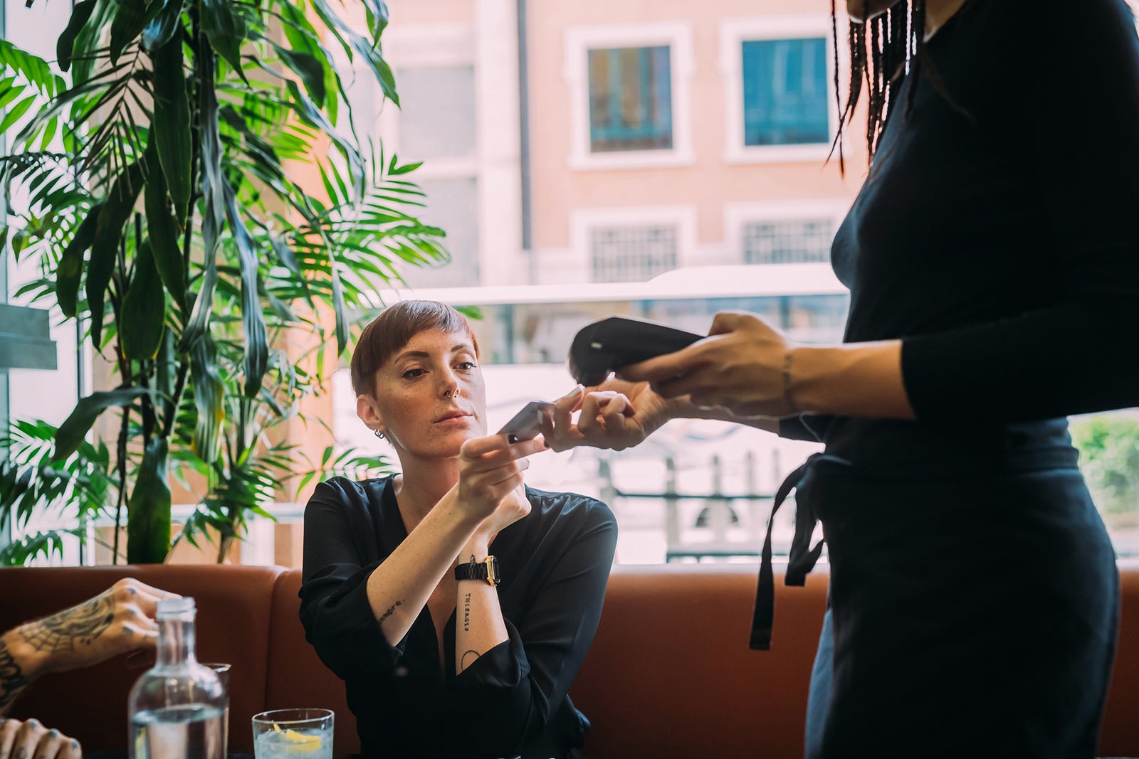 Young woman with short hair sitting in a bar, using credit card to pay.